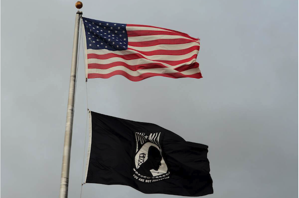 Photo of American flag flying over black and white POW_MIA flag.